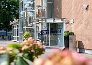 Art Hotel Aachen, Eingangsbereich, Eingangsbereich des Art Hotel Aachen mit Blumen im Vordergrund., Eingangsbereich des Art Hotel Aachen mit blühenden Pflanzen.