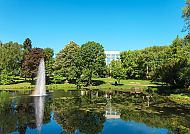 Sheraton Essen Hotel, Außenansicht, Sheraton Essen Hotel hinter grünem Park und Teich mit Springbrunnen.