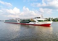 Flusskreuzfahrtschiff auf ruhigem Wasser unter blauem Himmel.